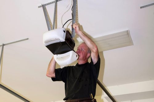 Man standing on a ladder fixing a mechanical garage door opener